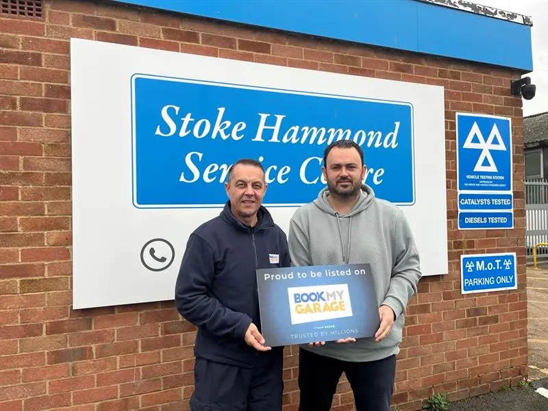 BookMyGarage employee stood next to owner of S H Service Centre in front of garage sign holding BookMyGarage branded card.